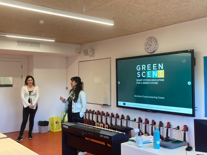 Two women are standing, behind them a big screen with the greenscent logo